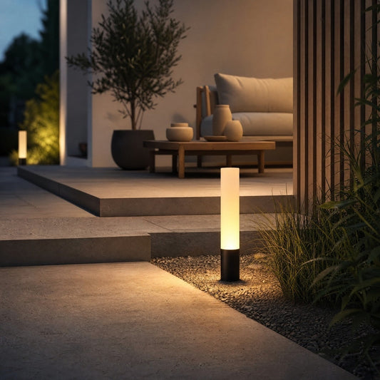 Black architectural outdoor lighting fixture casting warm pool on patio near wooden wall