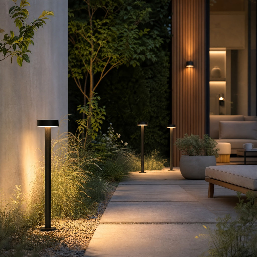 Black matte cylindrical outdoor ground light with flat disc top casting warm up-down glow on stone patio