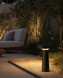Black outdoor garden stake lamp casting warm glow on ornamental grasses beside modern patio at night