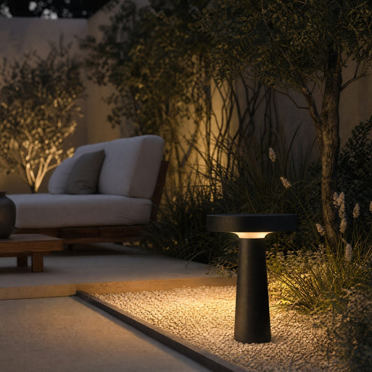 Black outdoor garden stake lamp casting warm glow on ornamental grasses beside modern patio at night