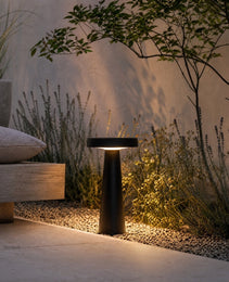 Black matte low-voltage LED ground light in garden with warm glow on gravel and lavender