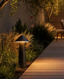 Black matte cone garden stake lamp illuminating ornamental grasses on wooden deck