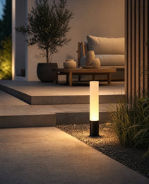 Black architectural outdoor lighting fixture casting warm pool on patio near wooden wall