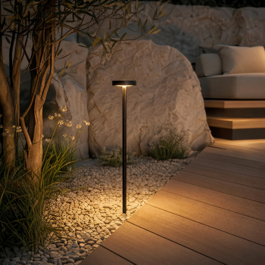 Black outdoor bollard light casting ambient warm white glow on gravel patio and stone boulders for residential landscape