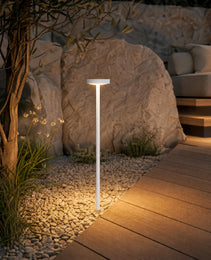 White IP65 rated outdoor bollard light illuminating garden path beside wooden deck at night with warm white glow