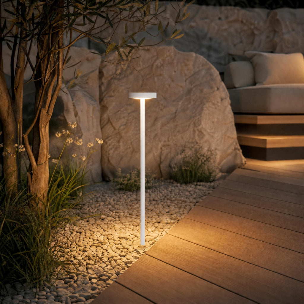 White IP65 rated outdoor bollard light illuminating garden path beside wooden deck at night with warm white glow