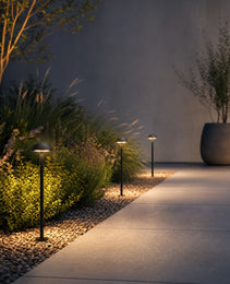 Matte black outdoor bollard lights casting warm glow along gravel walkway and shrubs