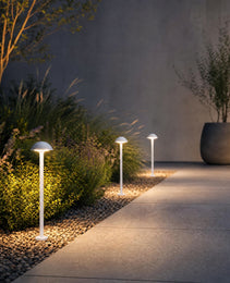 Three white dome bollard lights illuminating garden path with pebbles and ornamental grasses