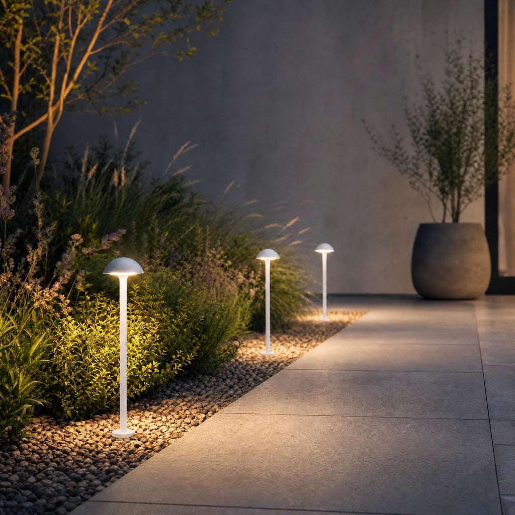 Three white dome bollard lights illuminating garden path with pebbles and ornamental grasses
