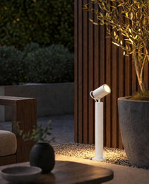 White outdoor bollard light with adjustable spot head on gravel patio