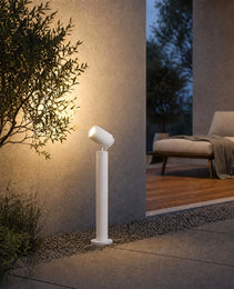 white outdoor bollard spotlight casting warm light on stucco wall and shrubs