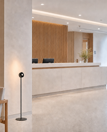 Black floor lamp in commercial lobby next to upholstered chair with warm wall glow