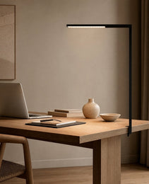 Black matte L-shaped floor lamp clipped to light wood desk in modern home office