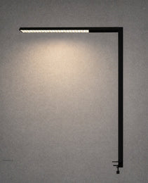 Black matte L-shaped desk lamp with visible adjustment knob against textured wall