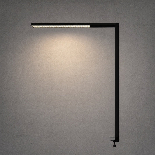 Black matte L-shaped desk lamp with visible adjustment knob against textured wall