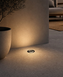 Dark matte DECK PRIME recessed floor light in concrete with warm glow beside olive tree for outdoor residential use