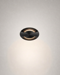 Oil-rubbed brass recessed floor light with curved cutouts and concentric machining details against textured wall