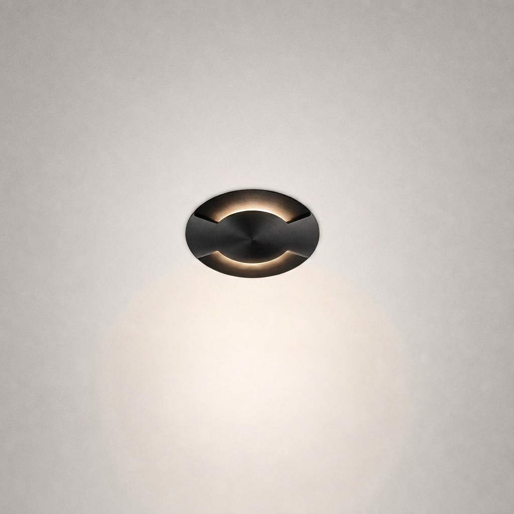 Oil-rubbed brass recessed floor light with curved cutouts and concentric machining details against textured wall