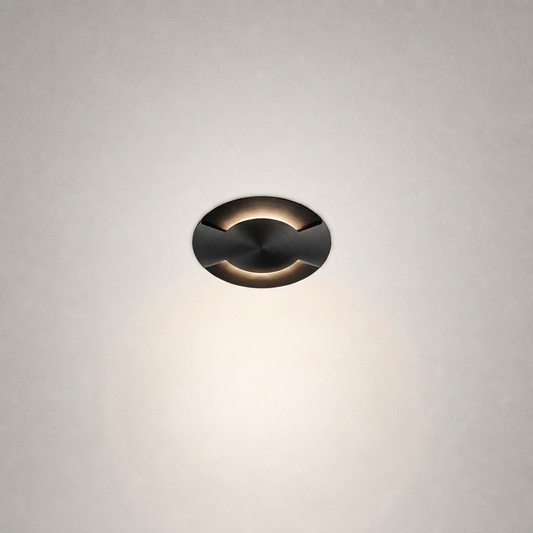 Oil-rubbed brass recessed floor light with curved cutouts and concentric machining details against textured wall