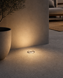 Polished brass DECK PRIME recessed floor light embedded in concrete casting soft pool of light for upscale outdoor spaces