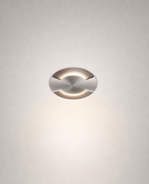 Brushed stainless steel circular recessed floor light flush mounted in gray wall showing minimalist architectural design