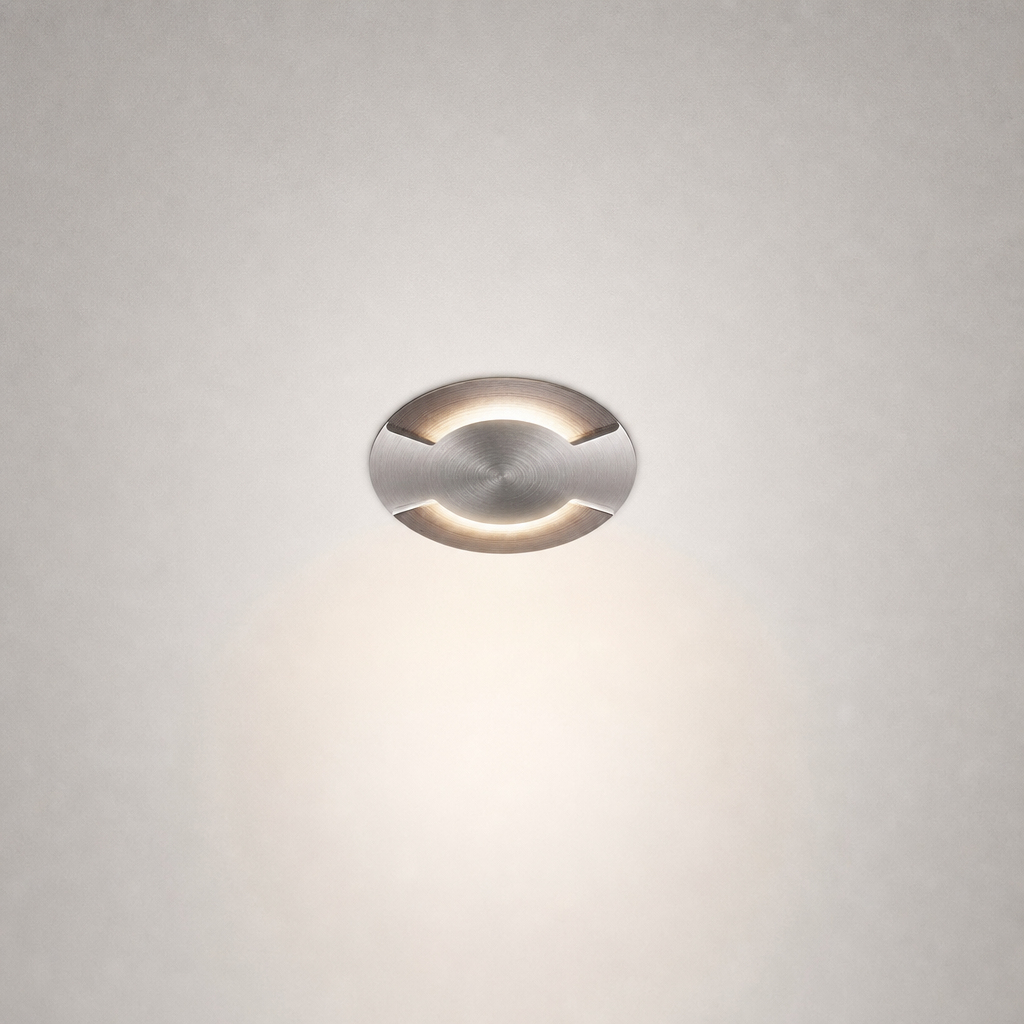 Brushed stainless steel circular recessed floor light flush mounted in gray wall showing minimalist architectural design