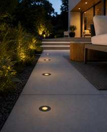 Black DECK PRIME 1168 pathway lights illuminating concrete patio at dusk