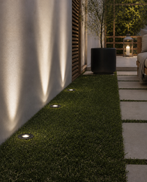 Dark matte black recessed outdoor spotlight DECK PRIME 1677 installed in artificial grass casting warm white light