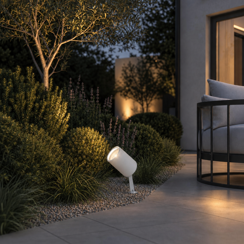 White matte outdoor spike lamp with angled head illuminating garden shrubs at dusk