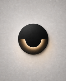 matte black circular recessed wall sconce with warm golden glow and geometric silhouette