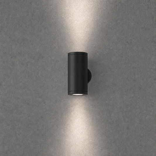 Close-up black matte finish cylindrical outdoor wall light with symmetrical up-down beams and circular backplate