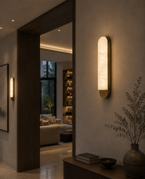 Vertical oval alabaster light fixture with warm glow mounted on hallway wall beside dark wood console