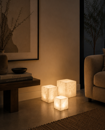 Set of three natural alabaster cube lamps with marbled texture on concrete floor next to woven rug